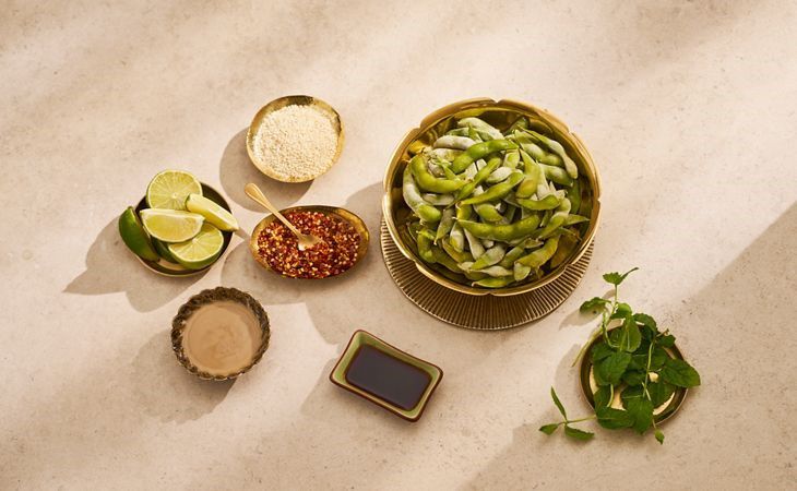 Eine Schüssel mit Edamame-Bohnen, Limette, Chiliflocken, Sesam und Sojasoße als gesunder proteinhaltiger Snack.