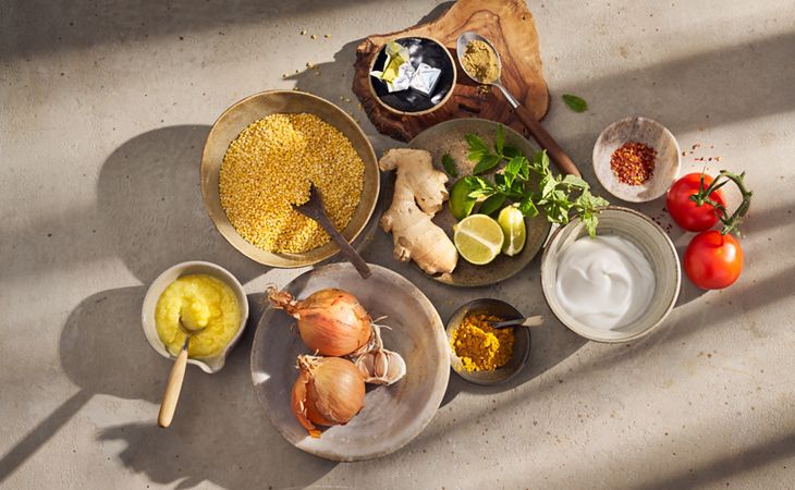 Ingredientes frescos para preparar una receta de kitchari ayurvédico, que incluye lentejas, cebolla, jengibre, leche de coco, lima y especias cálidas.