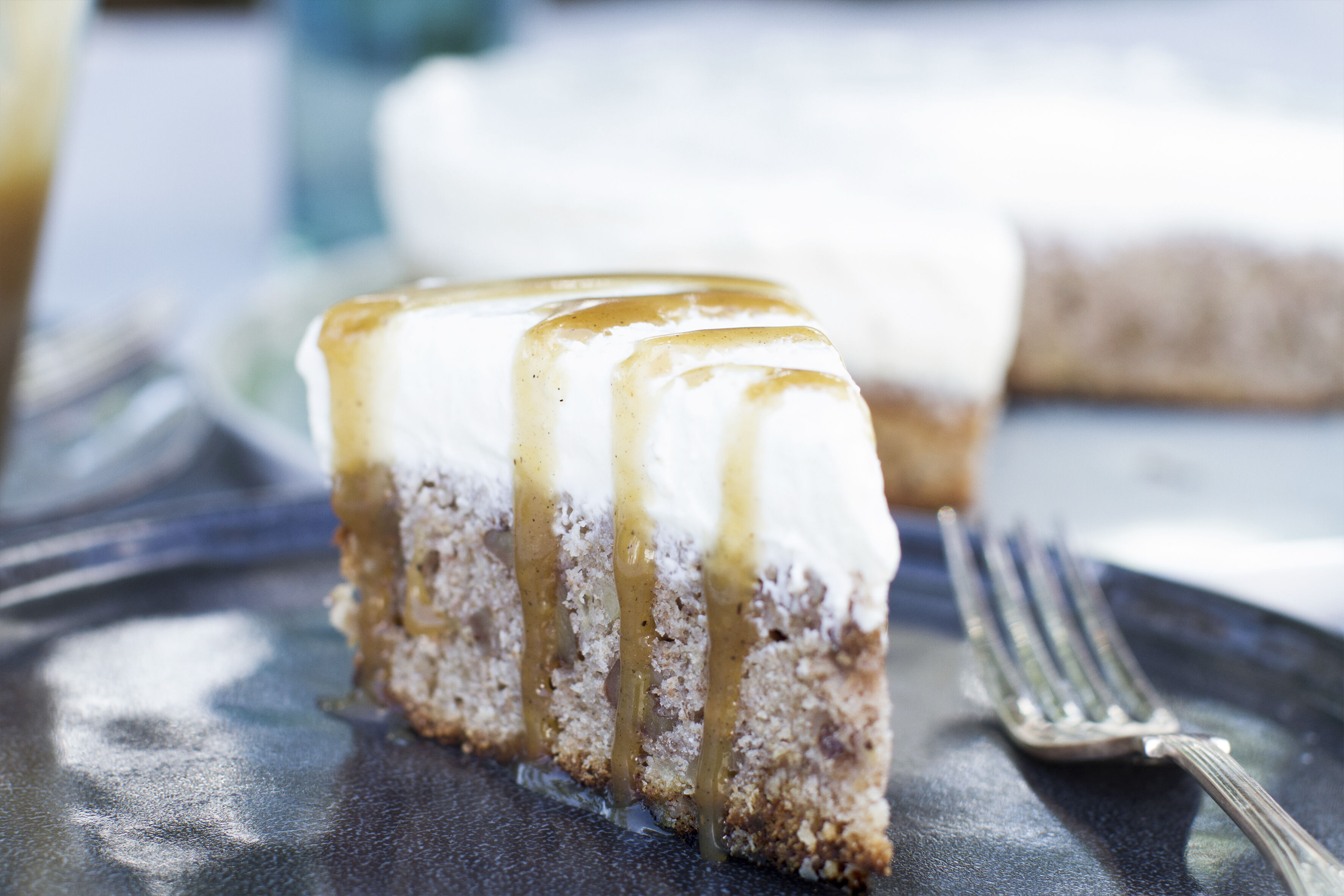 Slice of banana bread with cheesecake topping and caramel sauce served on a dark blue plate with a fork.