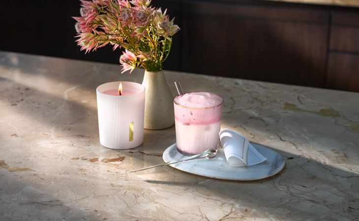 Cóctel sin alcohol y con espuma rosa, inspirado en The Ritual of Sakura, junto a una vela aromática a juego y un jarrón con flores.