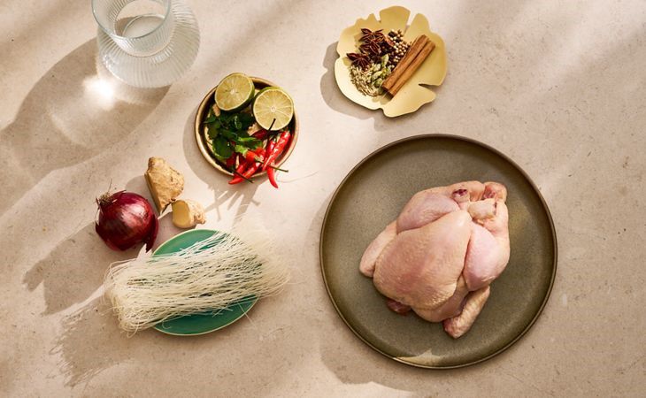 Fresh ingredients for homemade chicken pho, including a whole chicken, rice noodles, ginger, lime, chilli and spices.
