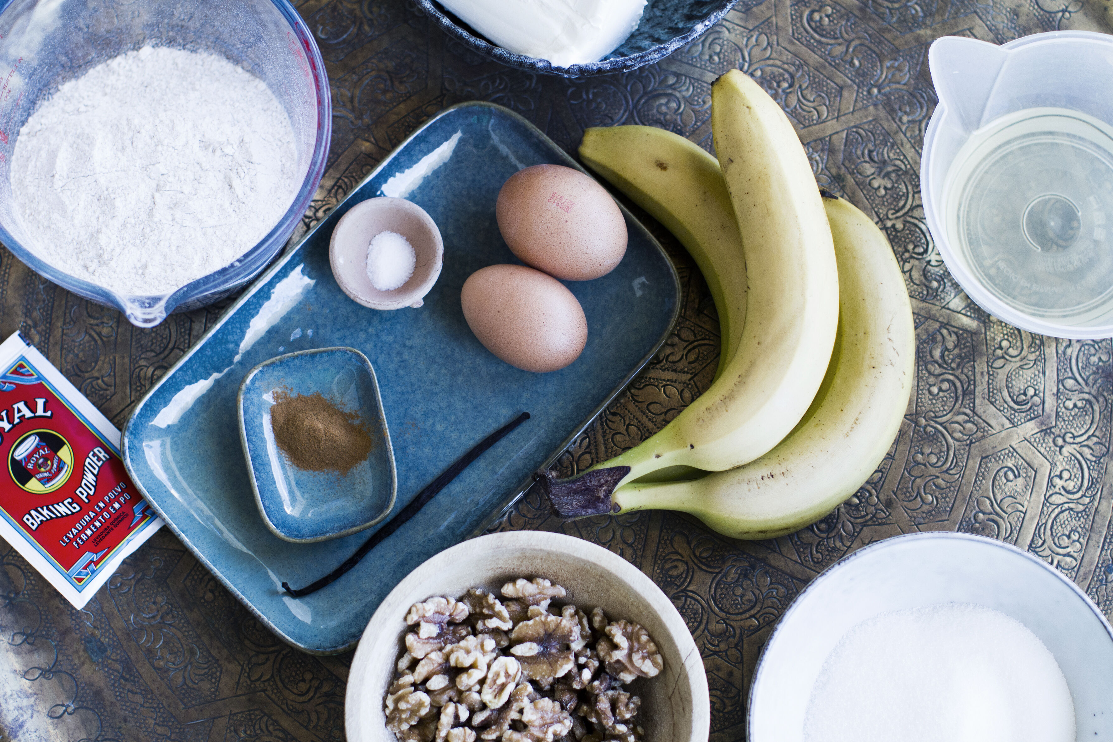 Banana cake ingredients including eggs, bananas, flour, walnuts and spices arranged on a table ready to bake.