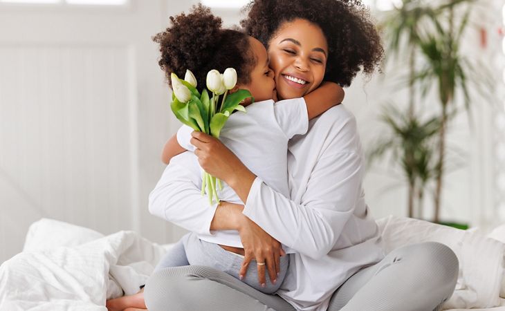 Eine lächelnde Mutter umarmt ihr Kind, das weiße Tulpen in der Hand hält – ein zärtlicher Moment der Liebe und Freundlichkeit.
