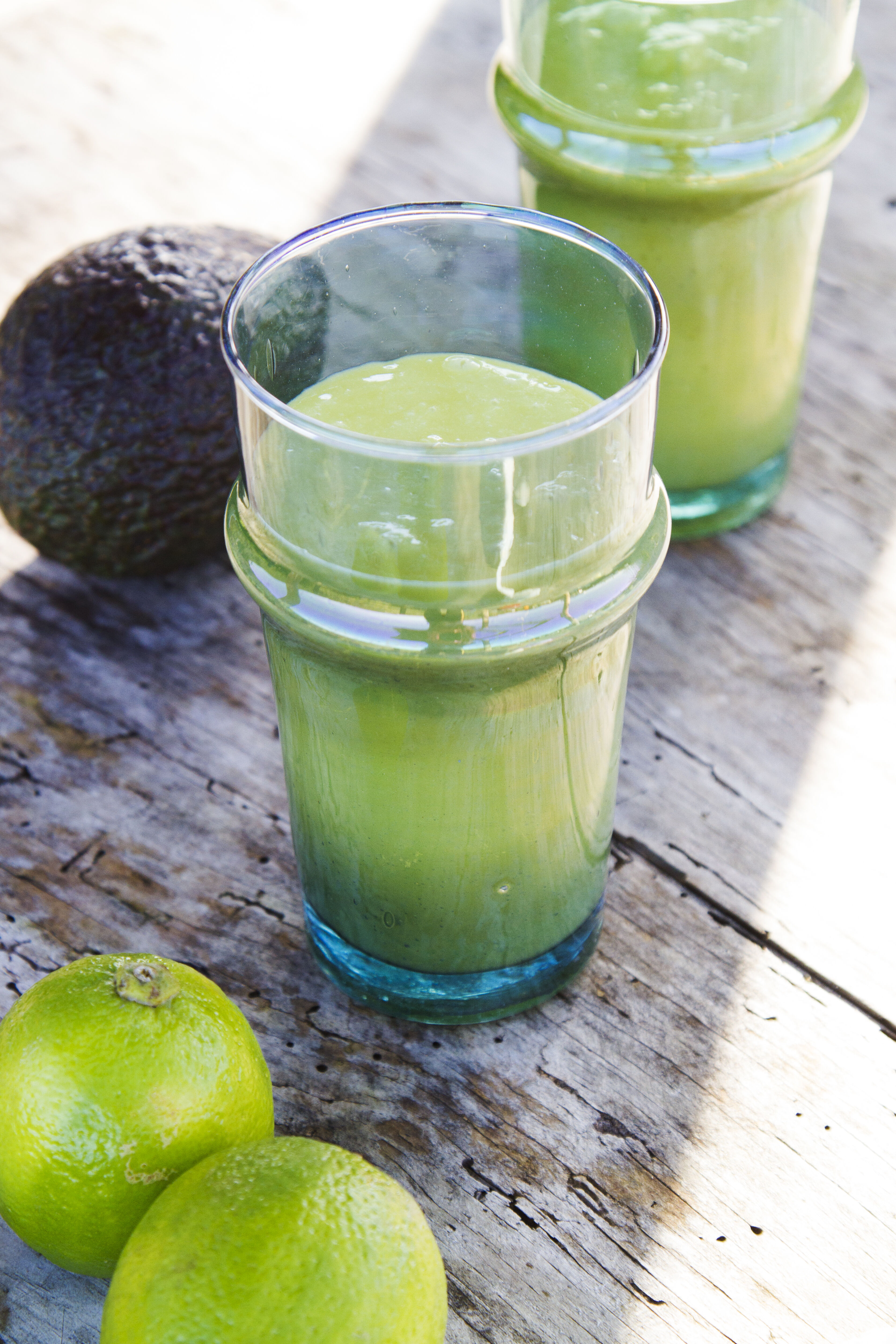 Ein Glas mit cremigem grünem Smoothie mit Avocado auf einer rustikalen Oberfläche – ein nahrhaftes Rezept für strahlende Haut.