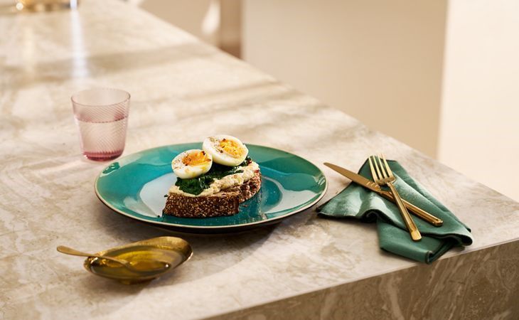 Vollkorntoast mit Hummus, Spinat und gekochtem Ei auf einem grünen Teller, eine gesunde und proteinreiche vegetarische Mahlzeit.