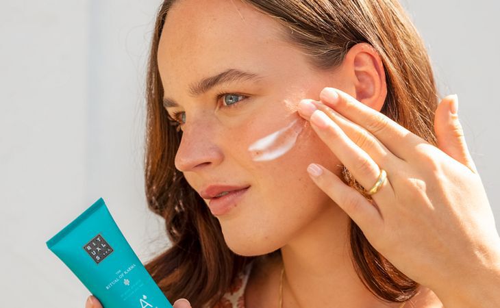 Femme appliquant le sérum après-soleil The Ritual of Karma sur son visage pour apaiser sa peau et la réhydrater après l’exposition au soleil.