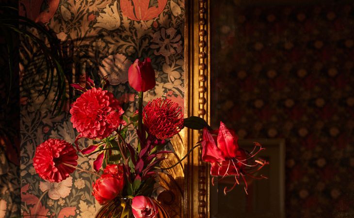 Un jarrón con flores rojas bañado en la luz cálida del atardecer que aporta lujo y elegancia dignos de un hotel a la decoración del hogar.