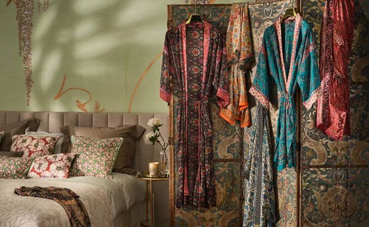Four House of Rituals silky kimonos featuring colourful decorative hand embroidery, shown hanging up in a cosy bedroom. 